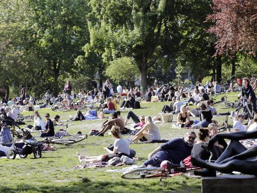 Menschen sitzen im Berliner Volkspark am Weinberg auf der Wiese, darunter viele junge Menschen, und genießen die sommerlichen Temperaturen bei Sonnenschein.