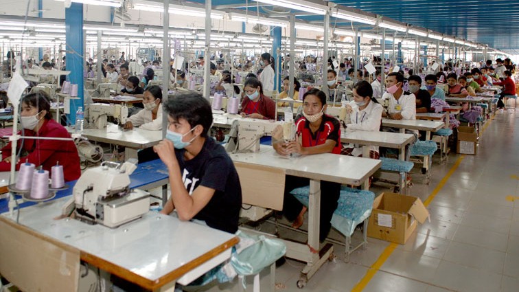 Kambodschanische Arbeiterinnen und Arbeiter sitzen im Jahr 2007 in einer Textilfabrik am Rande Phnom Penhs mit Mundschutz an Nähmaschinen.