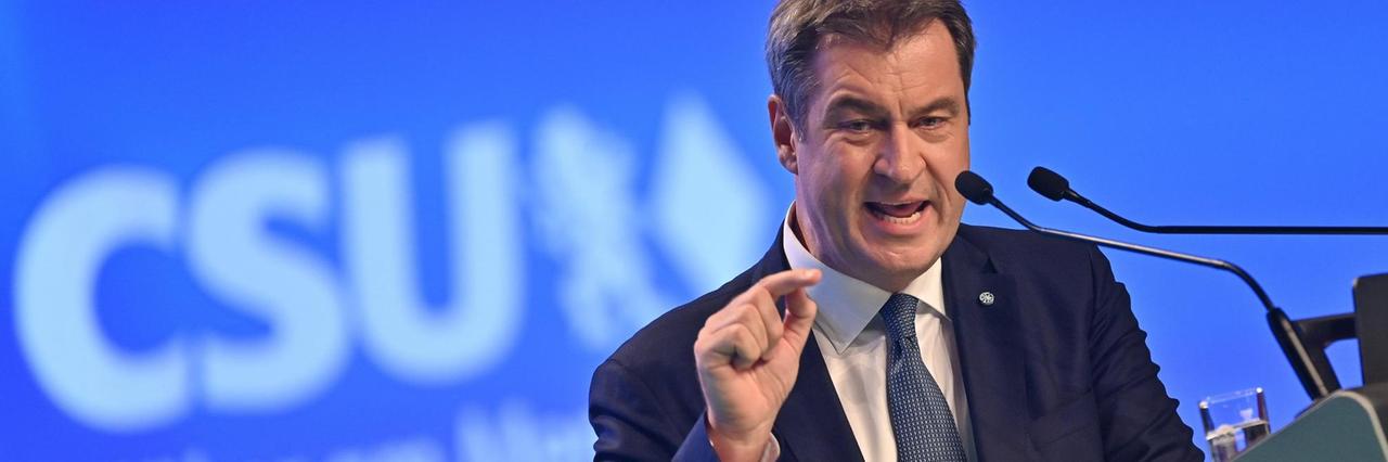 Markus Söder steht vor einem Mikrofon und spricht. Markus Söder steht vor einem Mikrofon und spricht.