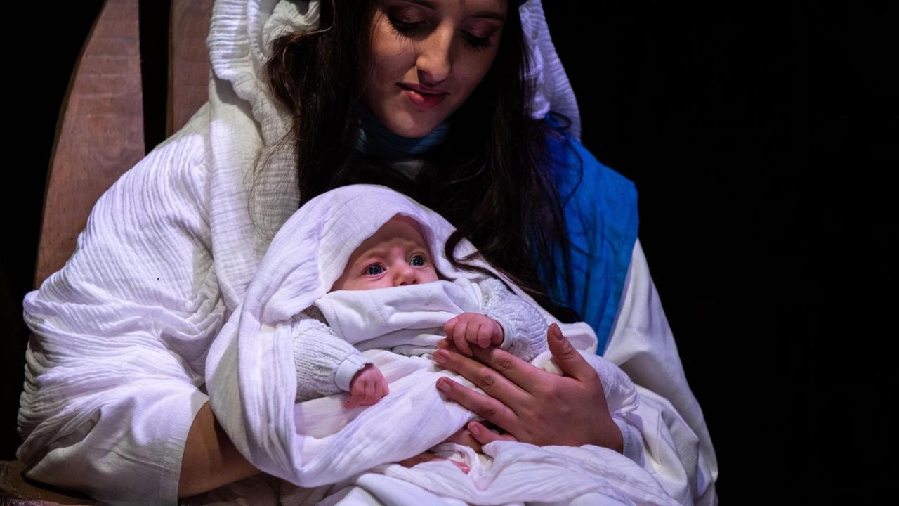 Eine Maria Darstellerin in einem biblischem Kostüm mit echtem Baby auf dem Schoß in einem Krippenspiel. Eine Maria Darstellerin in einem biblischem Kostüm mit echtem Baby auf dem Schoß in einem Krippenspiel.