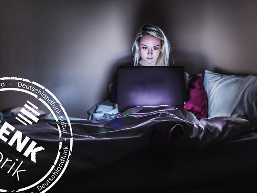 Eine Frau sitzt im Dunkeln in ihrem Bett und schaut auf ihren Laptop. (Mit Denkfabrik-Stempel)