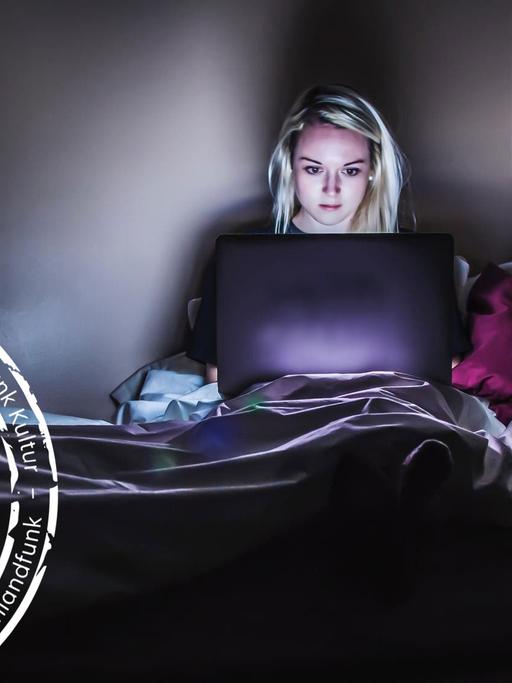 Eine Frau sitzt im Dunkeln in ihrem Bett und schaut auf ihren Laptop. (Mit Denkfabrik-Stempel)