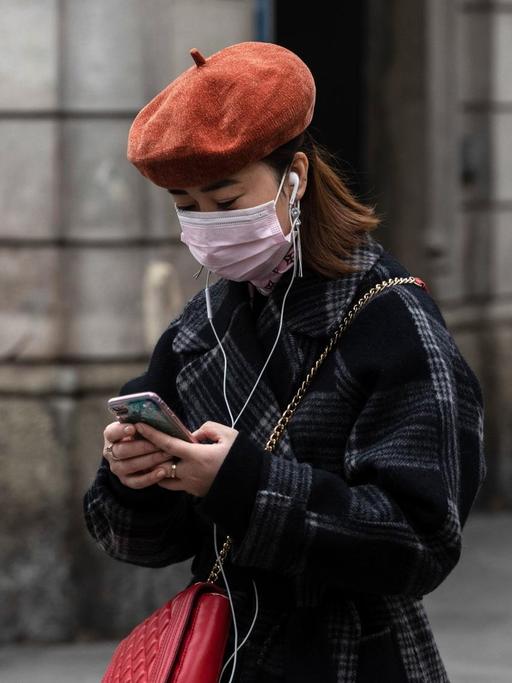 Eine Frau mit Atemmaske benutzt ihr Smartphone.