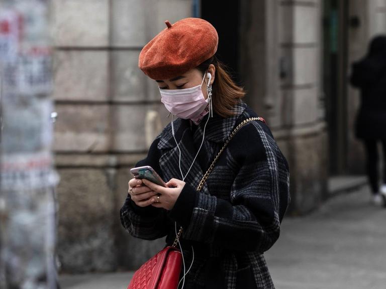 Eine Frau mit Atemmaske benutzt ihr Smartphone.