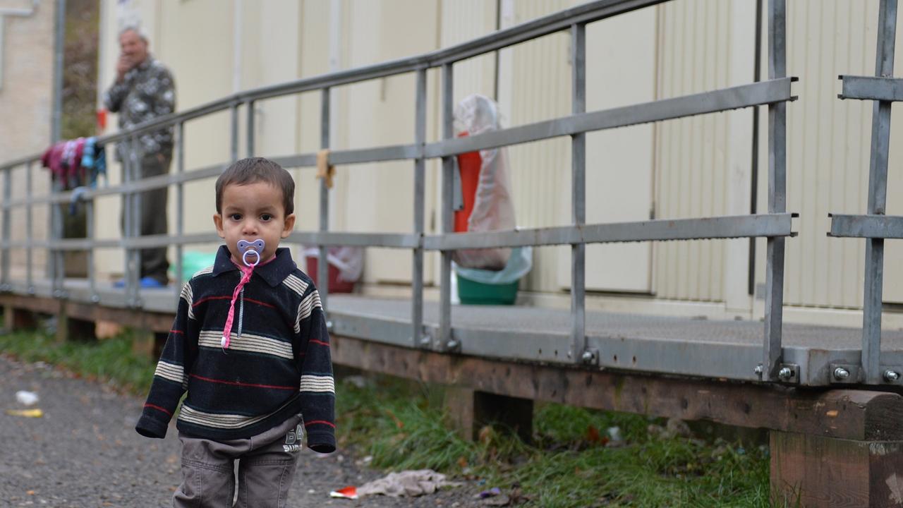 Ein Kleinkind steht am 21.11.2013 in Eisenberg (Thüringen) auf dem Gelände der Erstaufnahmestelle für Flüchtlinge und Asylbewerber vor Wohncontainern. Die Suche nach einer neuen Erstaufnahmestelle für Flüchtlinge in Thüringen gestaltet sich weiterhin schwierig. Es sei noch keine Entscheidung gefallen, sagte ein Sprecher des Innenministeriums der Nachrichtenagentur dpa in Erfurt. Ein Kleinkind steht am 21.11.2013 in Eisenberg (Thüringen) auf dem Gelände der Erstaufnahmestelle für Flüchtlinge und Asylbewerber vor Wohncontainern. Die Suche nach einer neuen Erstaufnahmestelle für Flüchtlinge in Thüringen gestaltet sich weiterhin schwierig. Es sei noch keine Entscheidung gefallen, sagte ein Sprecher des Innenministeriums der Nachrichtenagentur dpa in Erfurt.