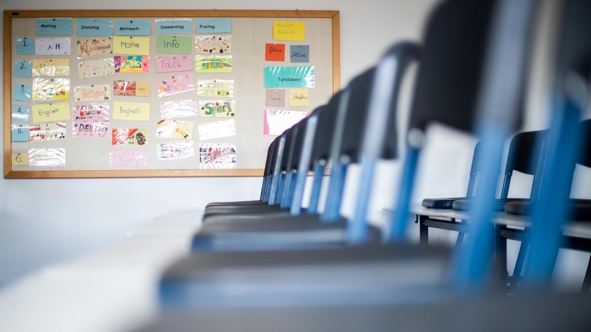 Nordrhein-Westfalen, Übach-Palenberg: Stühle stehen in einem leeren Klassenzimmer auf den Tischen, während im Hintergrund ein Stundenplan zu sehen ist. Nordrhein-Westfalen, Übach-Palenberg: Stühle stehen in einem leeren Klassenzimmer auf den Tischen, während im Hintergrund ein Stundenplan zu sehen ist.