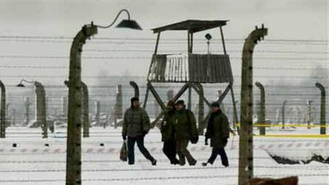 Männer gehen hinter dem Stacheldrahtzaun des früheren Nazi-Konzentrationslagers Auschwitz-Birkenau entlang