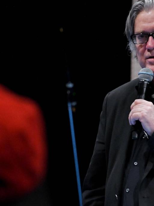 Steve Bannon mit Brille und einem Mikrofon in der Hand