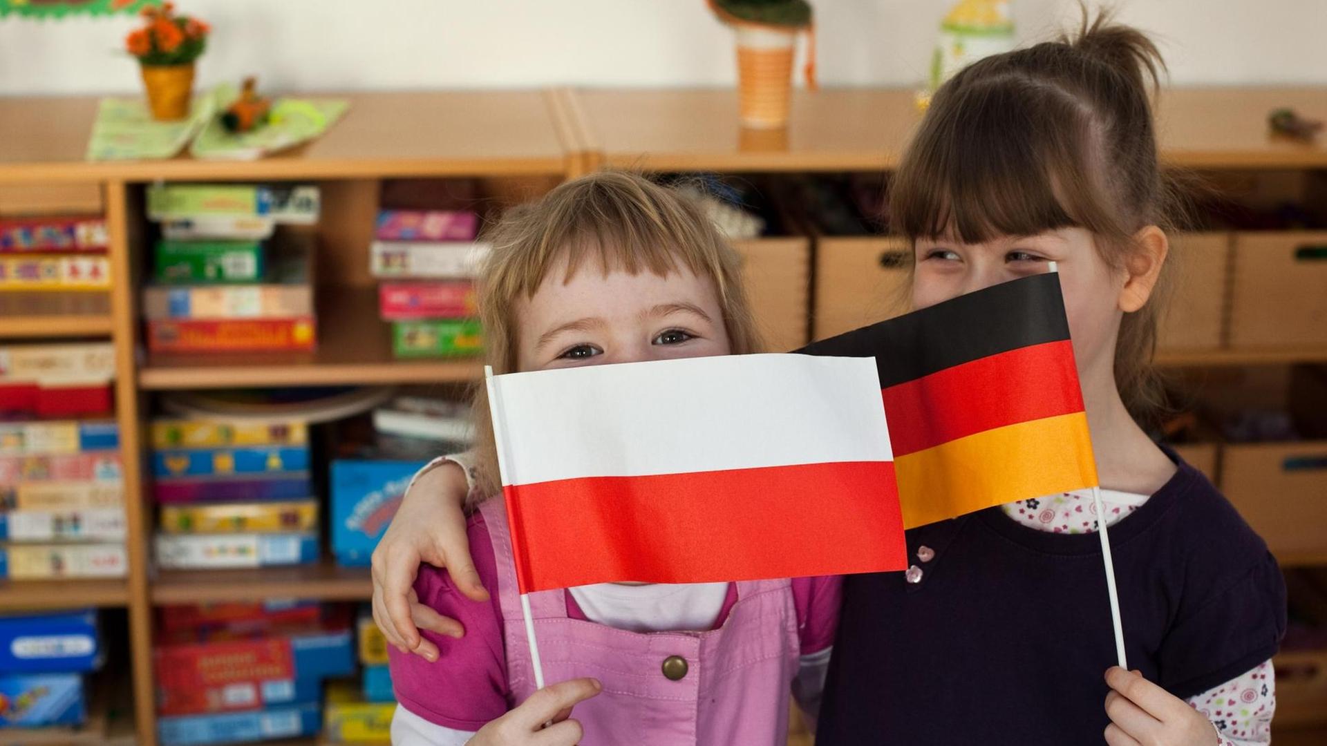 Die beiden Kinder haben sich im Arm und schwenken Papierfähnchen ihrer Länder. Die beiden Kinder haben sich im Arm und schwenken Papierfähnchen ihrer Länder.