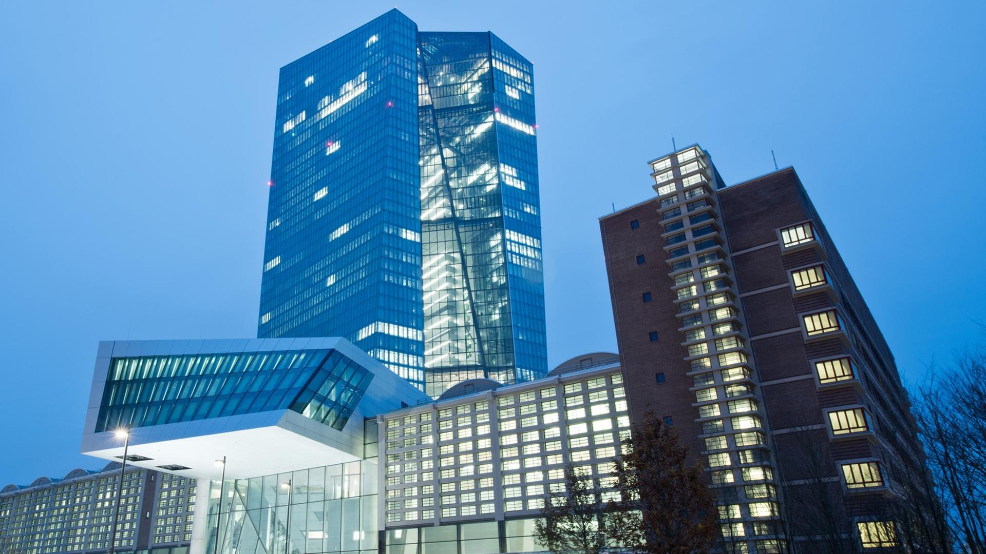 Außenansicht des EZB-Neubaus in Frankfurt in der Abenddämmerung. Hinter einem langgestreckten Gebäude erhebt sich ein gewundener Turm. Außenansicht des EZB-Neubaus in Frankfurt in der Abenddämmerung. Hinter einem langgestreckten Gebäude erhebt sich ein gewundener Turm.