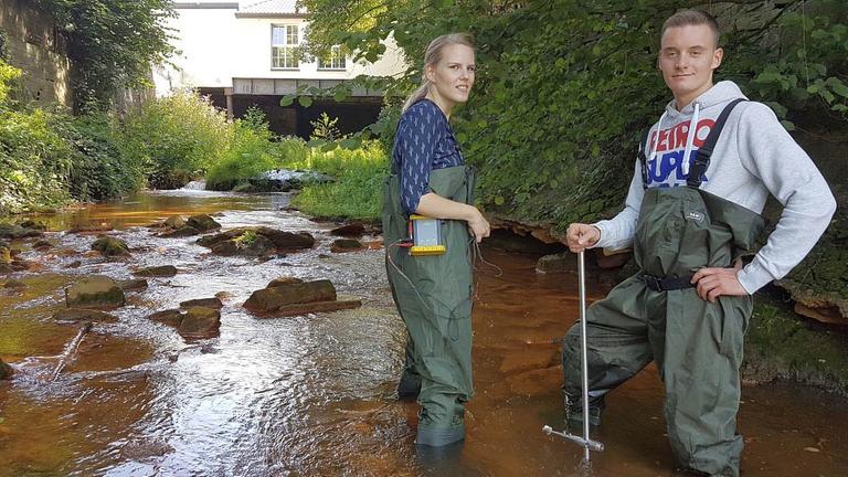 Carmen Tomlik und Marco Bischoff stehen in grünen Anglerhosen im Wasser. Carmen Tomlik und Marco Bischoff stehen in grünen Anglerhosen im Wasser.