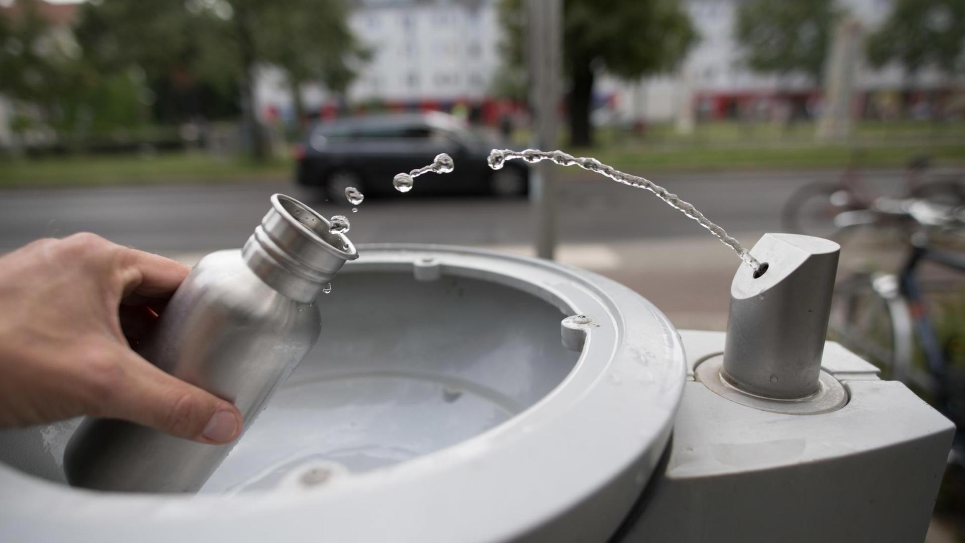 An einem Wasserspender der Berliner Wasserbetriebe füllt sich ein Passant seine Trinkflasche mit Wasser auf.