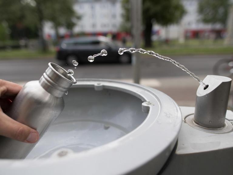 An einem Wasserspender der Berliner Wasserbetriebe füllt sich ein Passant seine Trinkflasche mit Wasser auf.