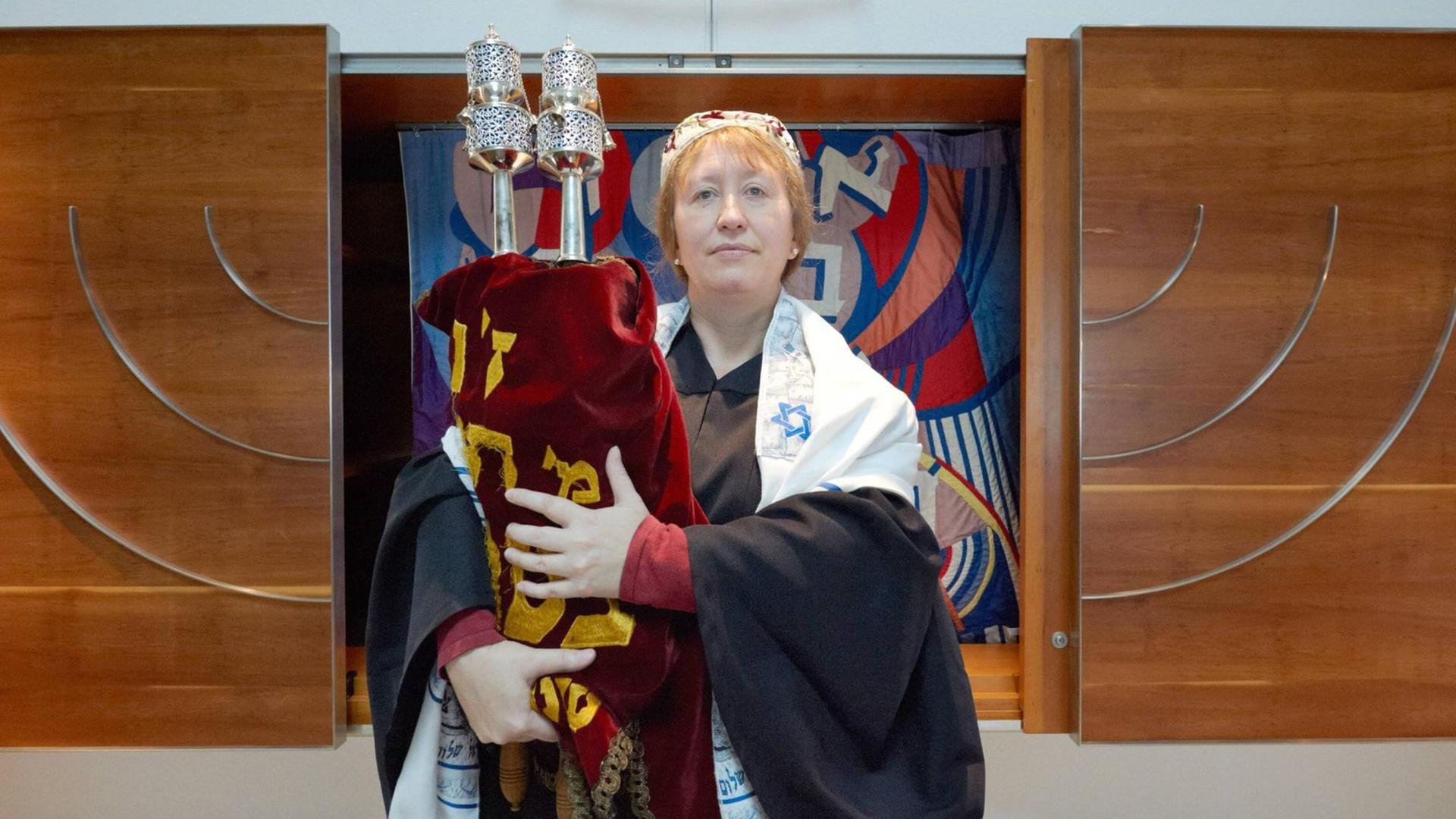 Antje Yael Deusel steht mit der Tora ein einer nüchtern eingerichteten Synagoge. Antje Yael Deusel steht mit der Tora ein einer nüchtern eingerichteten Synagoge.