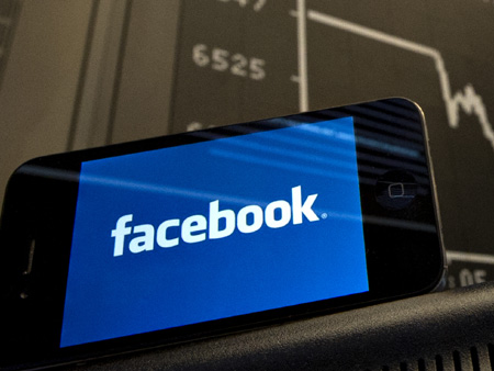 Ein Smartphone zeigt das Facebook-Logo vor einer Anzeigetafel der Dax-Kurve