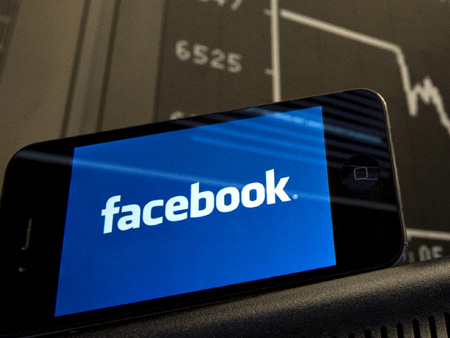 Ein Smartphone zeigt das Facebook-Logo vor einer Anzeigetafel der Dax-Kurve Ein Smartphone zeigt das Facebook-Logo vor einer Anzeigetafel der Dax-Kurve
