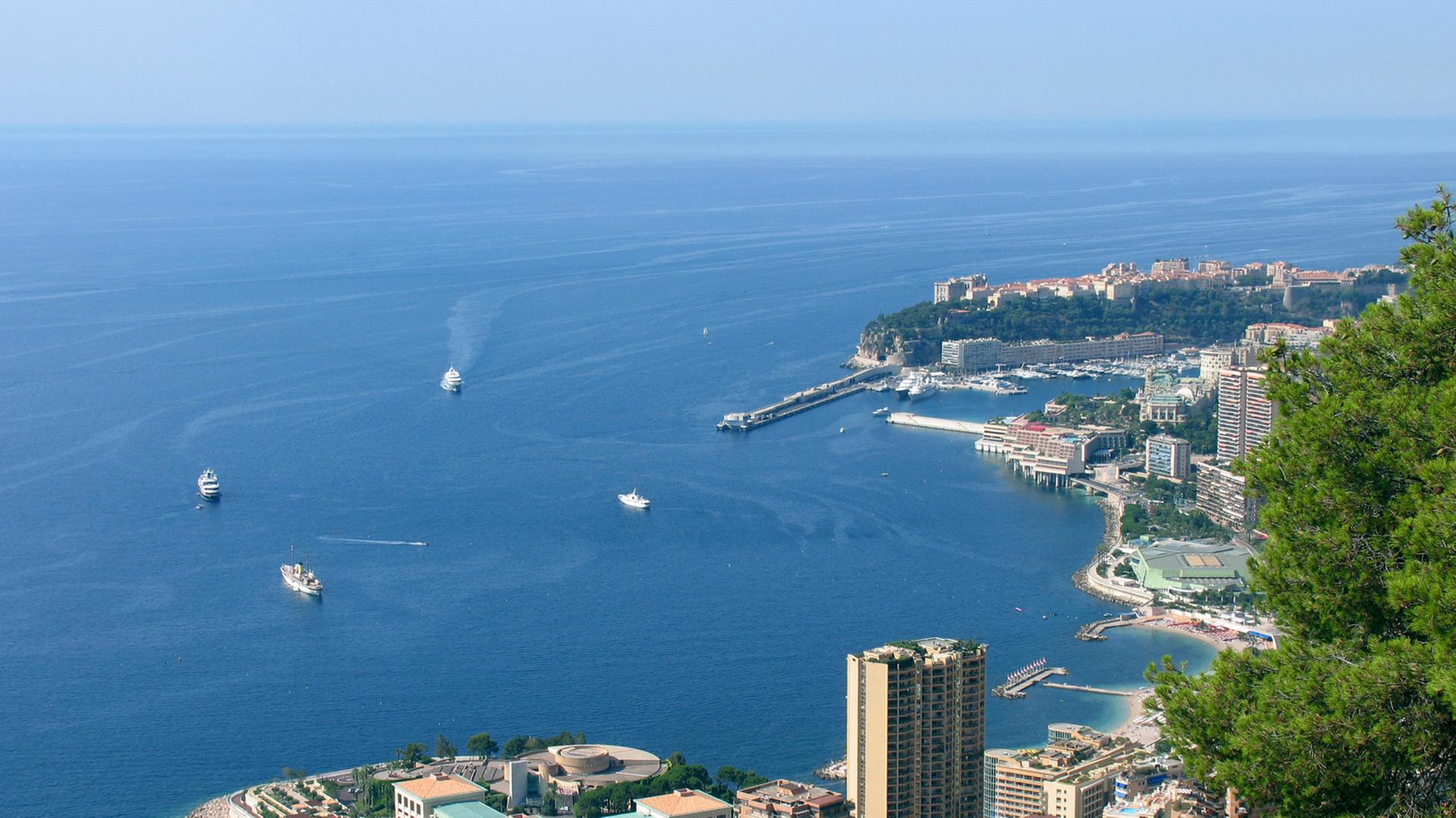 Blick auf Monte Carlo mit dem Casino im Vorder- und dem Yachthafen im Hintergrund. Am Berg hinten Monaco Ville mit Fürstenpalast und Meeresaquarium.