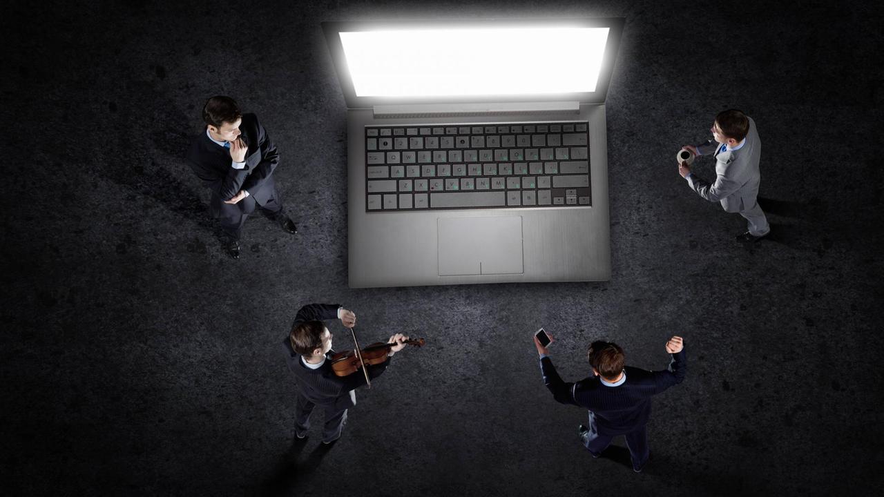 Vier Personen stehen um einen überdimensionierten Laptop und sind dem Bildschirm zugewandt. Einer spielt Geige, die anderen hören mehr oder weniger konzentriert zu. Vier Personen stehen um einen überdimensionierten Laptop und sind dem Bildschirm zugewandt. Einer spielt Geige, die anderen hören mehr oder weniger konzentriert zu.