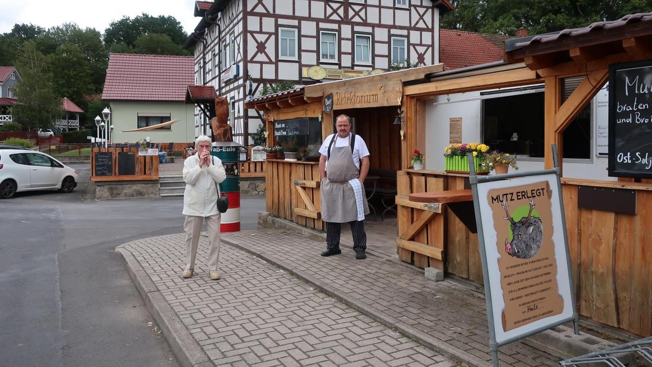 Ein Wirt steht mit Schürze auf dem Gehsteig vor seinem Imbiss. Ein Wirt steht mit Schürze auf dem Gehsteig vor seinem Imbiss.