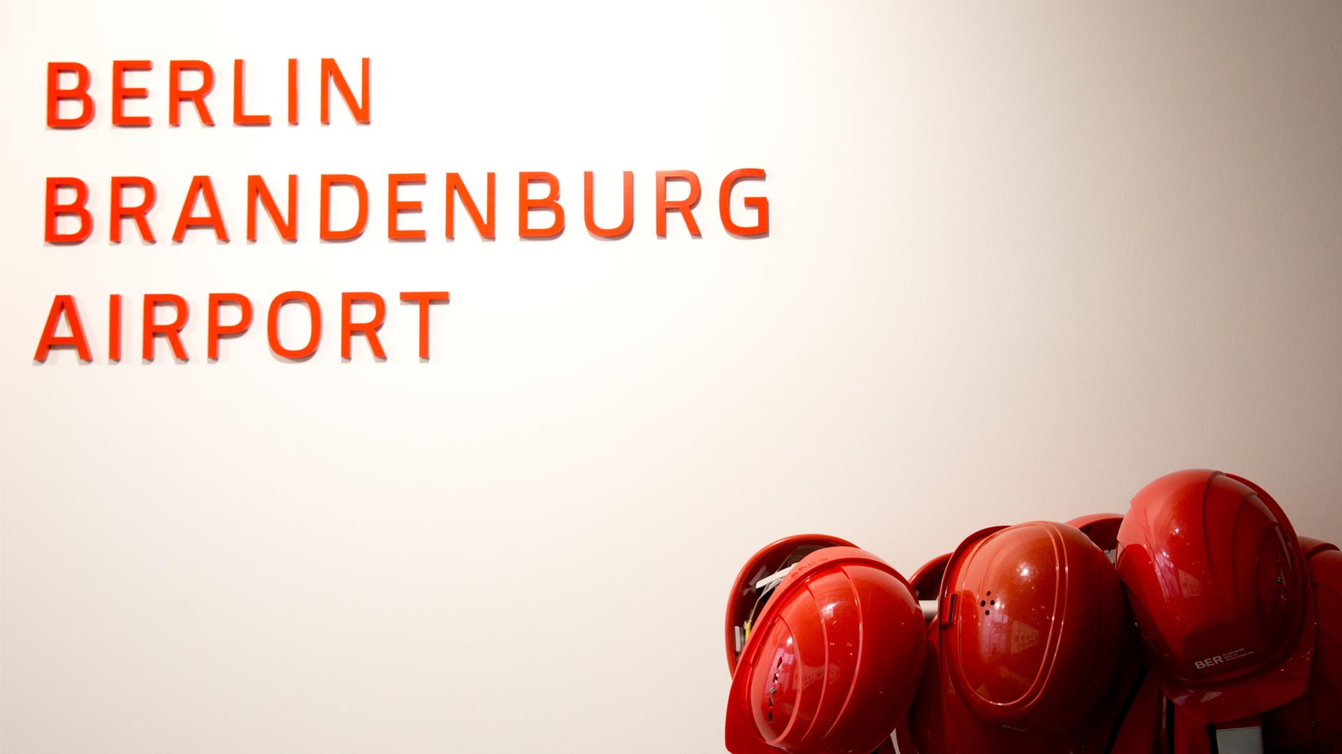 Bauarbeiterhelme und - jacken hängen neben dem Logo des Berliner Flughafens BER Bauarbeiterhelme und - jacken hängen neben dem Logo des Berliner Flughafens BER