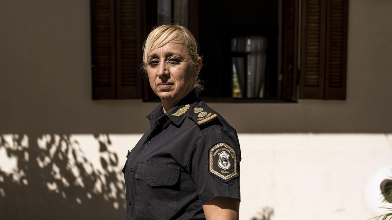 Eine blonde Frau mit Abzeichen am dunklen kurzärmligen Hemd steht in der Sonne vor einem Haus. Eine blonde Frau mit Abzeichen am dunklen kurzärmligen Hemd steht in der Sonne vor einem Haus.