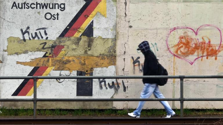 Ein Passant geht am 30.03.2012 an einer Schallschutzmauer in Magdeburg an einem aus der Wendezeit stammenden verwitterten Wandbild mit dem Schriftzug «Gemeinschaftswerk Aufschwung Ost» vorbei. 