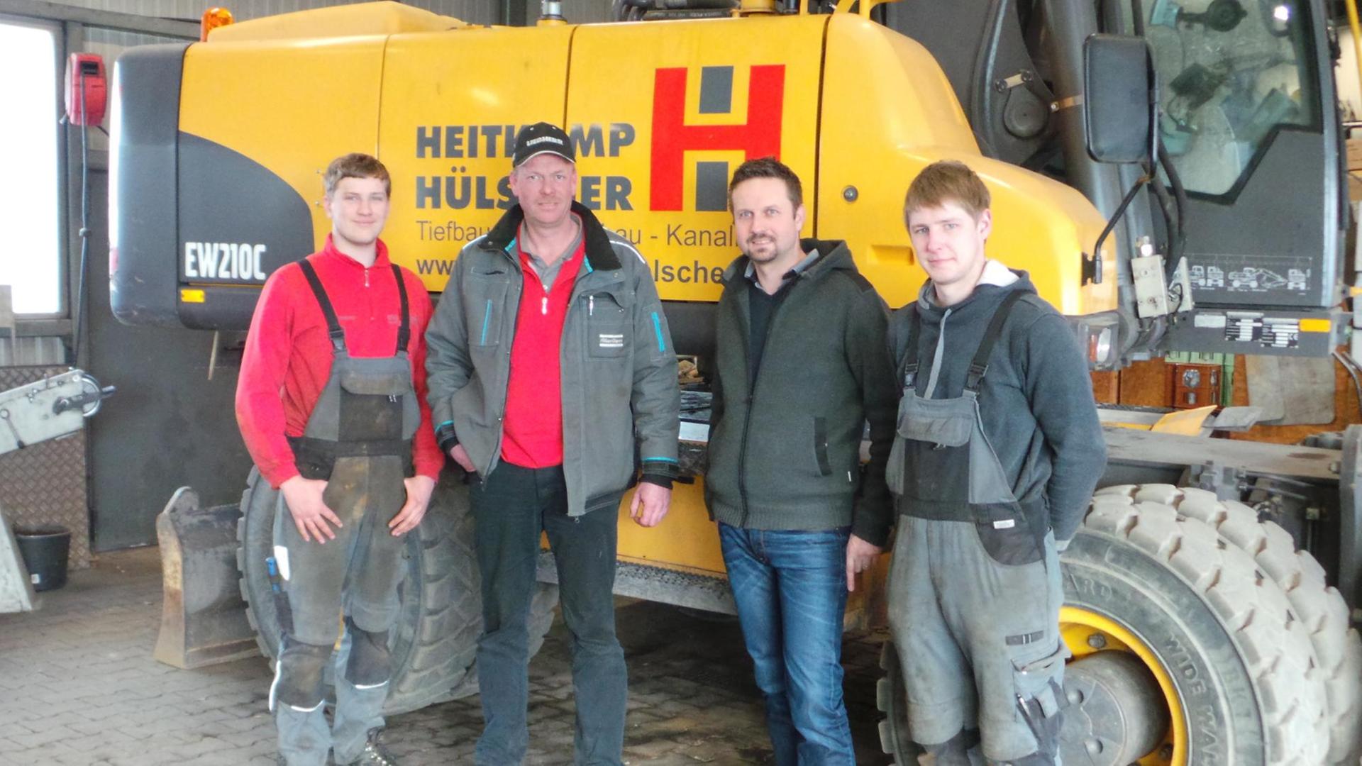 Mitarbeiter des Bauunternehmens Heitkamp & Hülscher stehen vor einem Bagger. Sie sind an dem Unternehmen beteiligt.