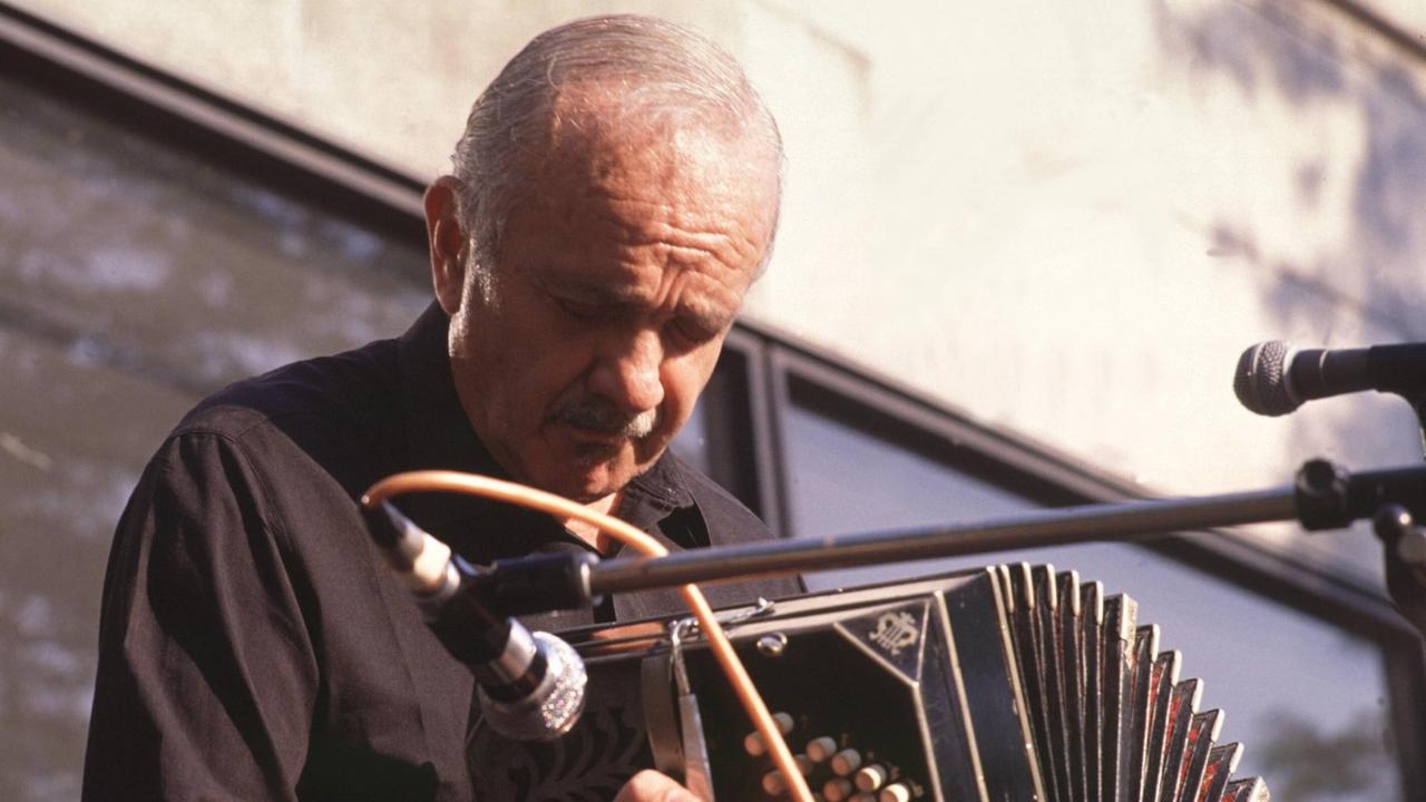 Ein Mann sitzt mit seinem Bandoneon vor einem Mikrofon und spielt vertieft. Ein Mann sitzt mit seinem Bandoneon vor einem Mikrofon und spielt vertieft.