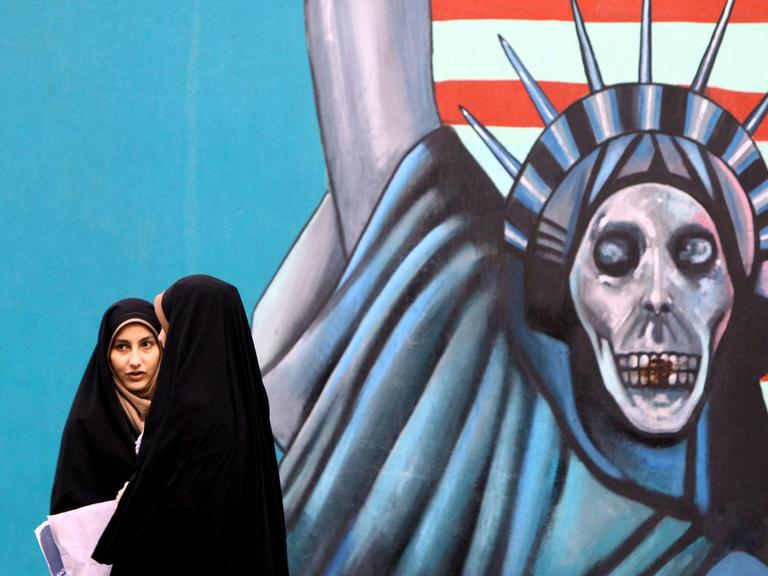 Zwei Schülerinnen mit Kopftüchern laufen an einem Wandbild vorbei. Das Bild zeigt die Freiheitsstatue mit Totenkopf statt Gesicht.