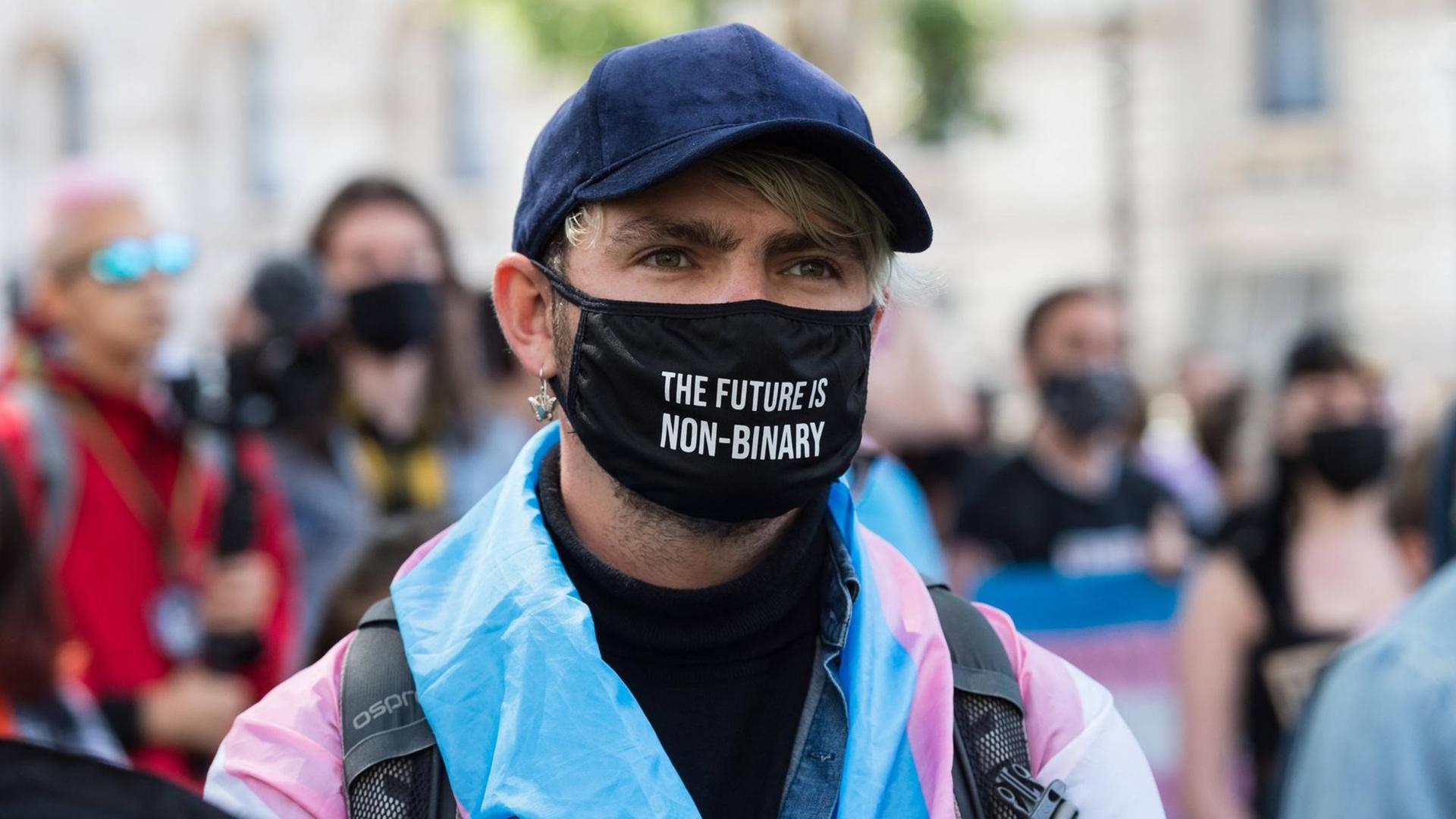 Demonstration für Transrechte in London. Ein junger Mensch trägt einen schwarzen Mundschutz mit der Aufschrift. "The future in non-binary". Demonstration für Transrechte in London. Ein junger Mensch trägt einen schwarzen Mundschutz mit der Aufschrift. "The future in non-binary".