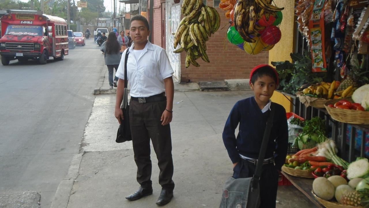 Junge in Schuluniform in Straße mit Gemüsestand