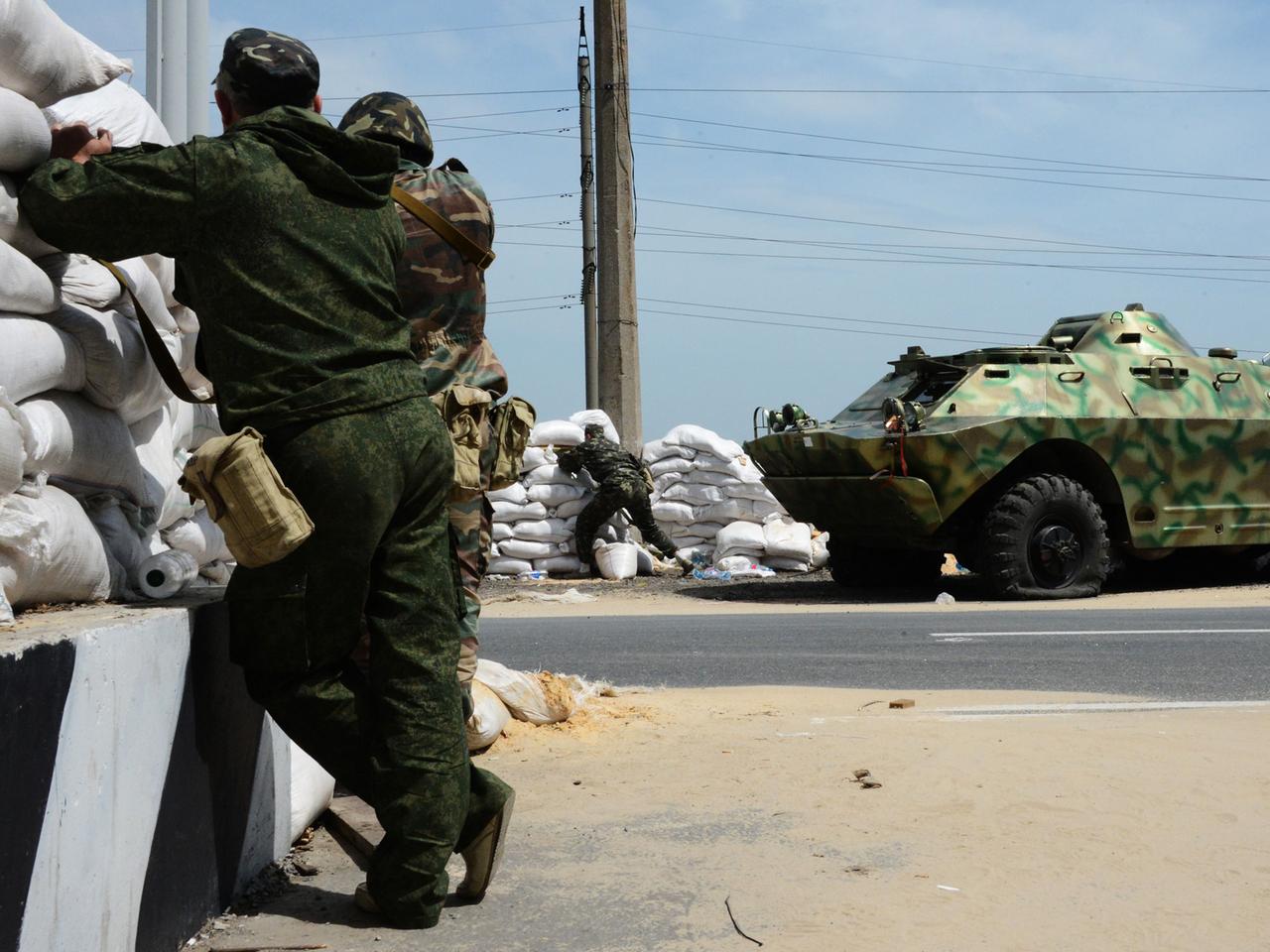 Zwei Kämpfer der Bevölkerungsmiliz des Donbass stehen an einem Checkpoint in der Nähe des Dorfes Peski in der Ost-Ukraine, im Hintergrund steht ein Panzer. Zwei Kämpfer der Bevölkerungsmiliz des Donbass stehen an einem Checkpoint in der Nähe des Dorfes Peski in der Ost-Ukraine, im Hintergrund steht ein Panzer.