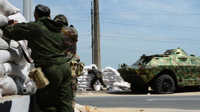Zwei Kämpfer der Bevölkerungsmiliz des Donbass stehen an einem Checkpoint in der Nähe des Dorfes Peski in der Ost-Ukraine, im Hintergrund steht ein Panzer.