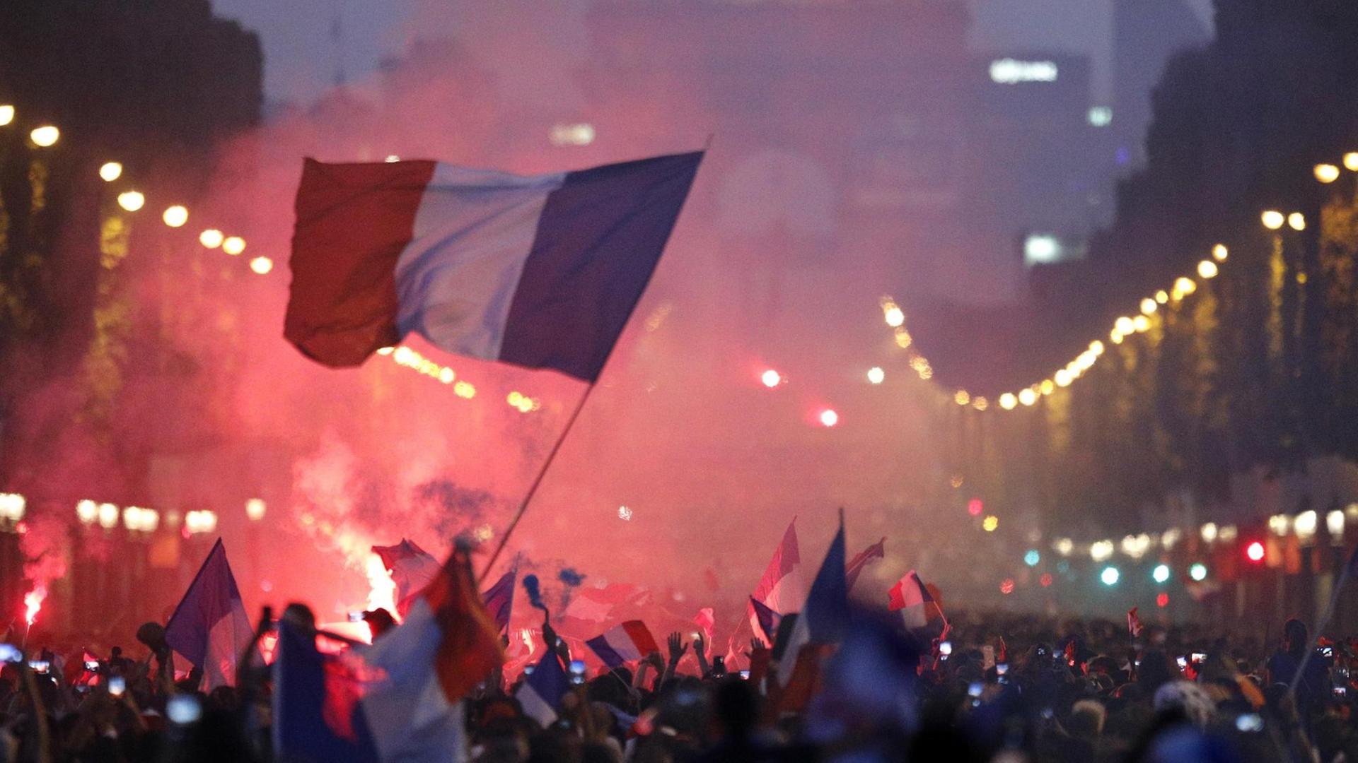 Fans von Frankreich feiern über den WM-Sieg auf den Champs-Elysees vor dem Arc de Triomphe und schwenken eine Nationalflagge.