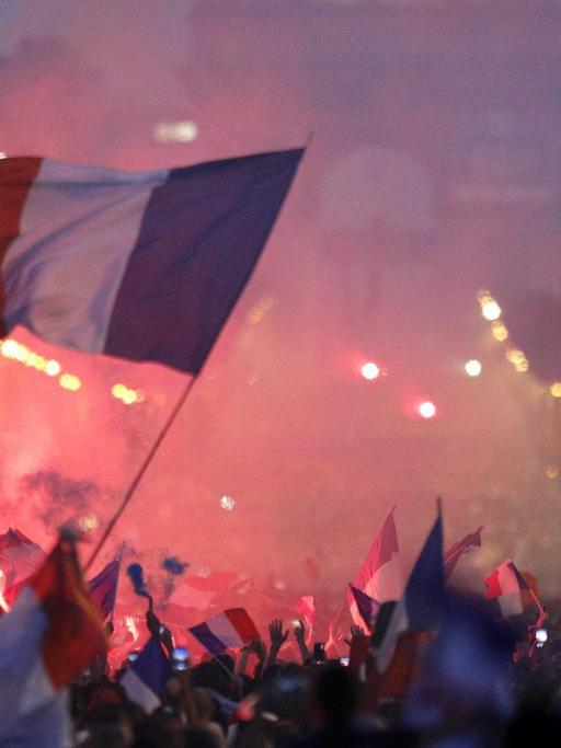 Fans von Frankreich feiern über den WM-Sieg auf den Champs-Elysees vor dem Arc de Triomphe und schwenken eine Nationalflagge.