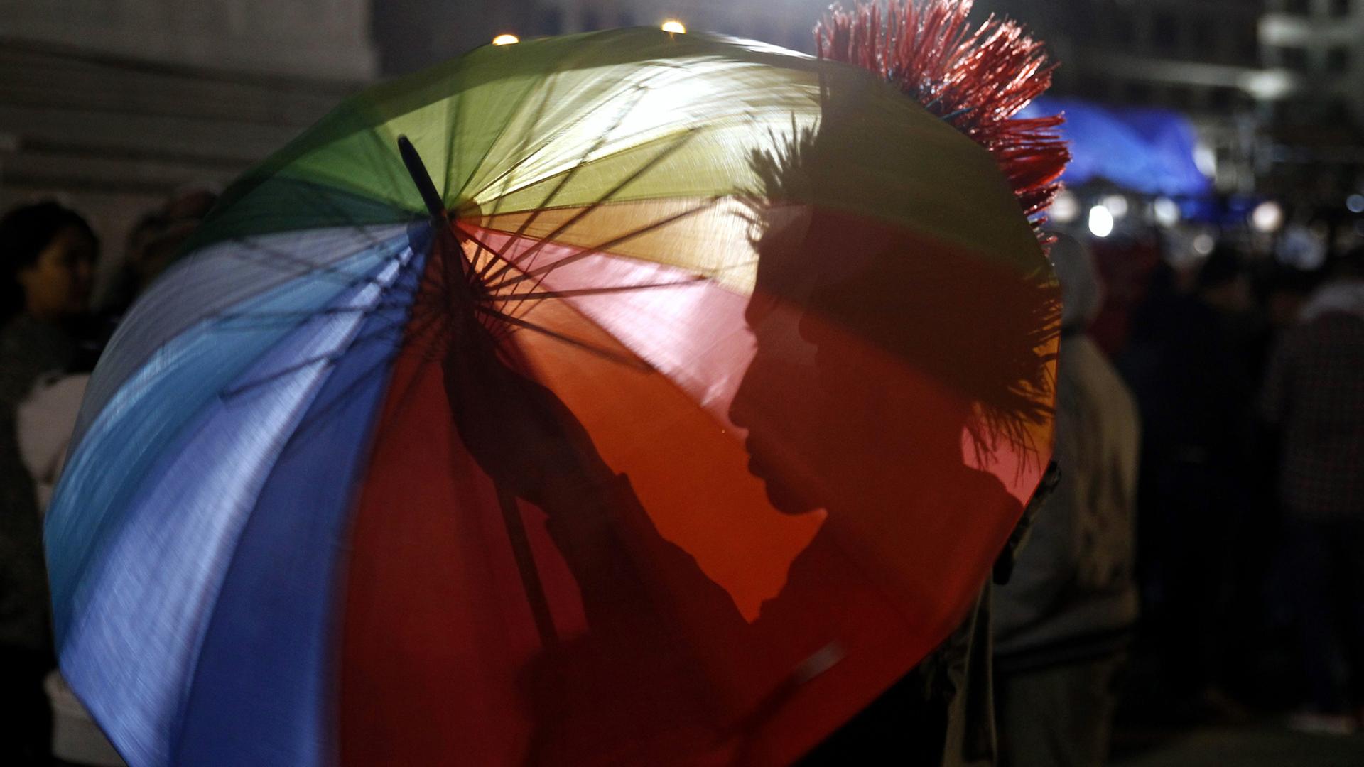 Demonstrant unter einem Regenschirm in Regenbogenfarben am LGTB-Tag 2016 in Montevideo, Uruguay Demonstrant unter einem Regenschirm in Regenbogenfarben am LGTB-Tag 2016 in Montevideo, Uruguay