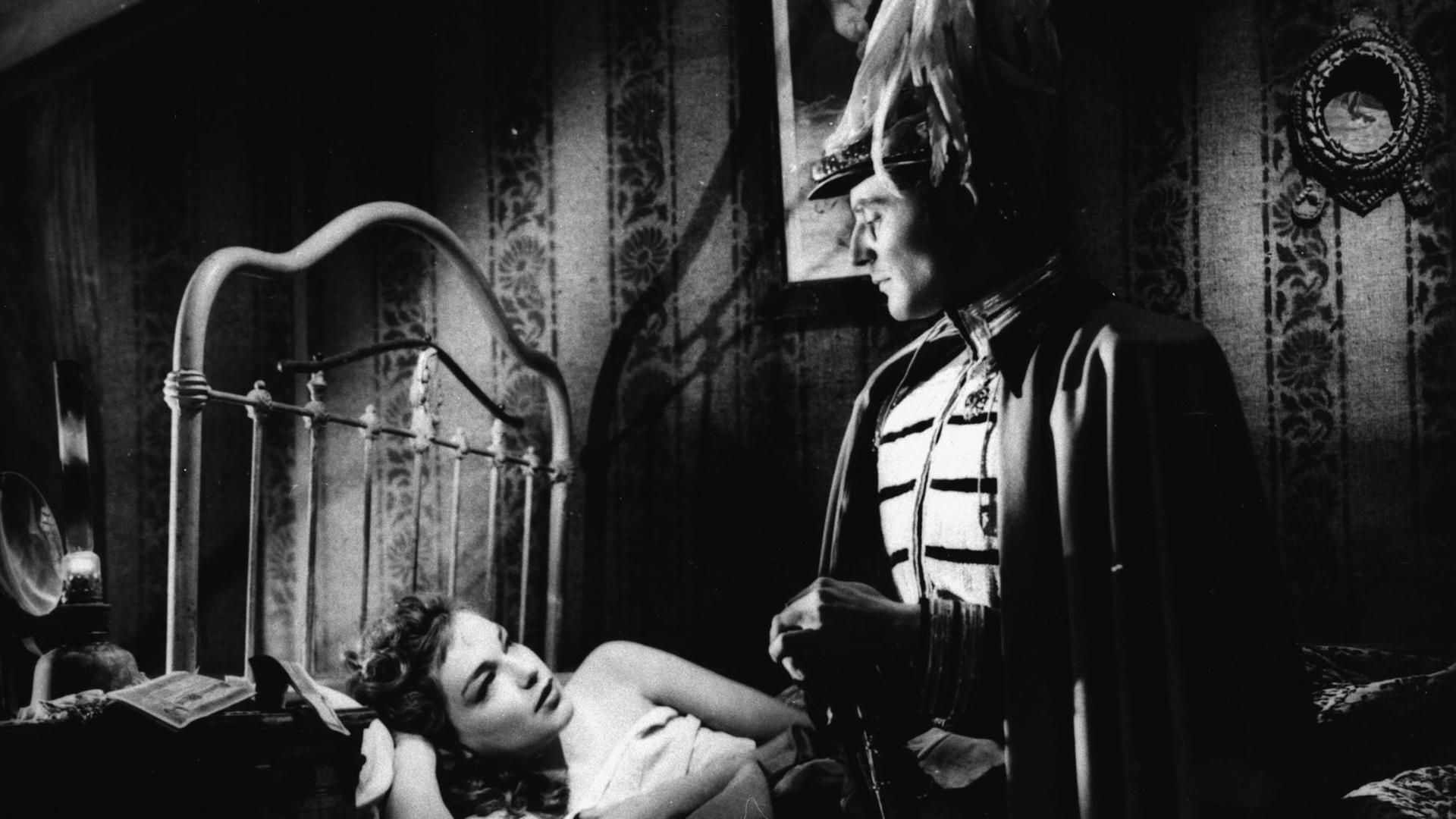 Ein schwarzweißes Filmstill aus Max Ophuels' Film "Der Reigen" (La Ronde) von 1950 zeigt eine Szene mit Gerard Philippe und Simone Signoret, ihn in Uniform stehend dieauf dem Bett liegende schmachtend anblickend Ein schwarzweißes Filmstill aus Max Ophuels' Film "Der Reigen" (La Ronde) von 1950 zeigt eine Szene mit Gerard Philippe und Simone Signoret, ihn in Uniform stehend dieauf dem Bett liegende schmachtend anblickend