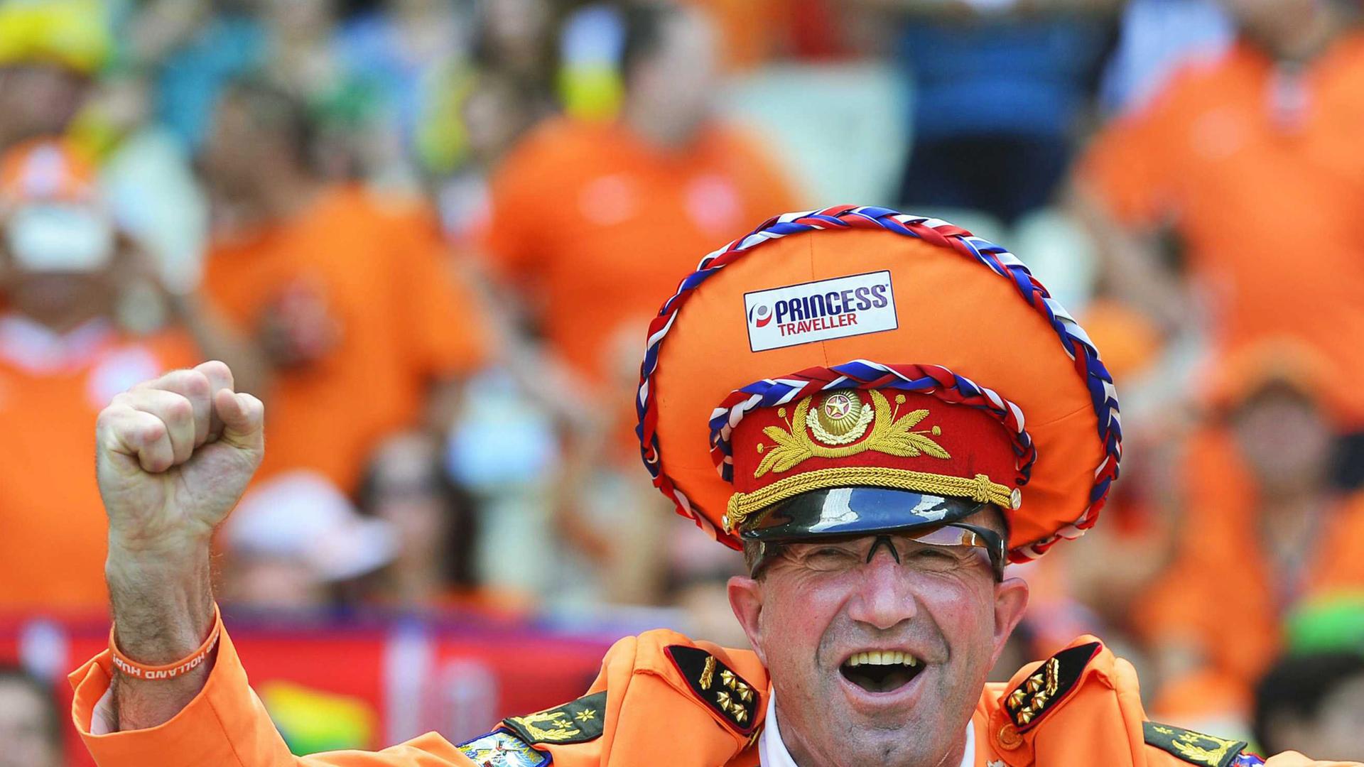 Niederländischer Fußballfan bei der Fußball-WM in Brasilien - mit orangener Mütze und Jacket und einer Fliege in den Farben der niederländischen Flagge. Er ballt siegesgewiss eine Faust. Niederländischer Fußballfan bei der Fußball-WM in Brasilien - mit orangener Mütze und Jacket und einer Fliege in den Farben der niederländischen Flagge. Er ballt siegesgewiss eine Faust.