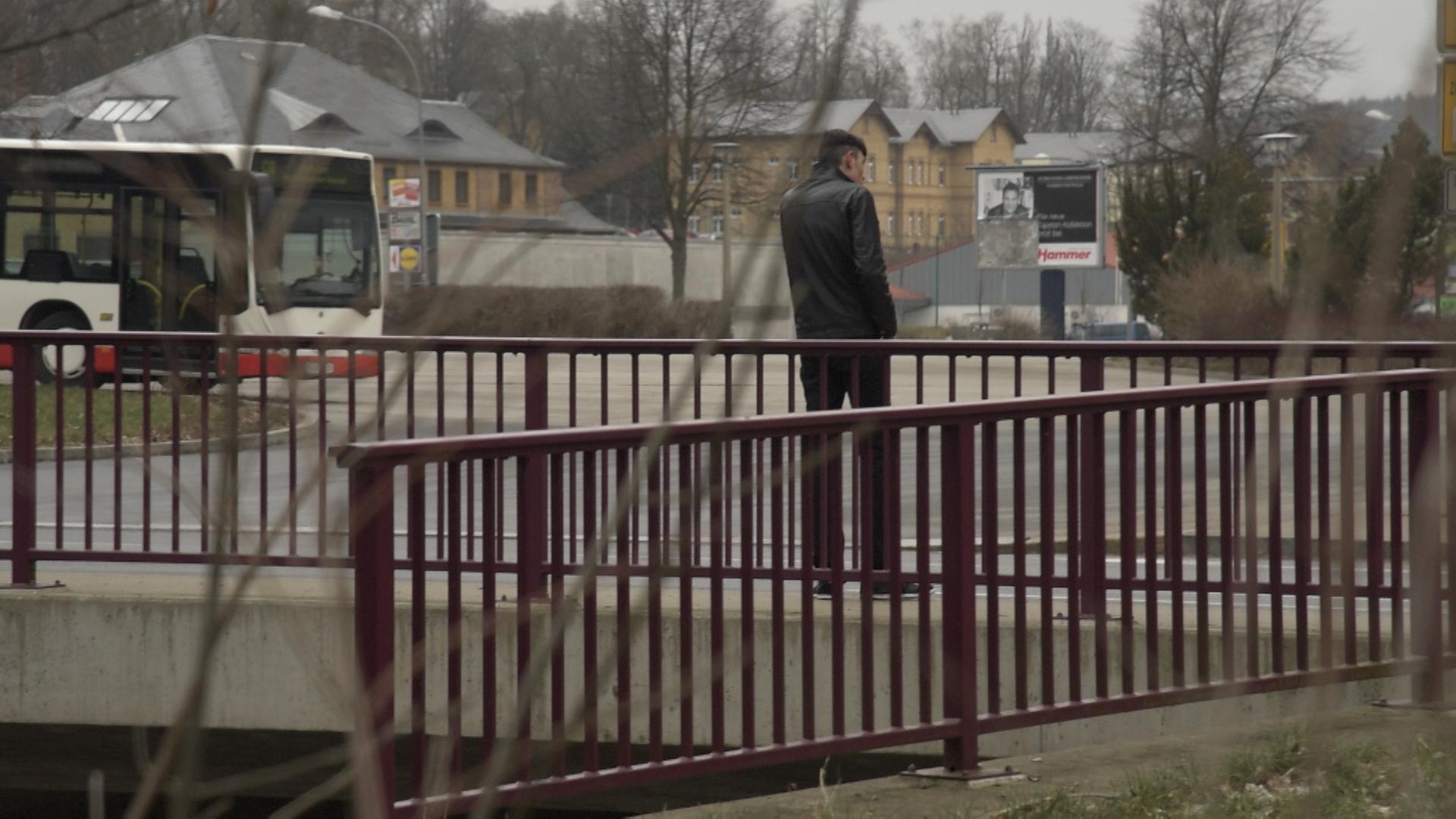 Ein junger Mann steht an einem Straßenrand, man sieht ihn von hinten. Ein junger Mann steht an einem Straßenrand, man sieht ihn von hinten.