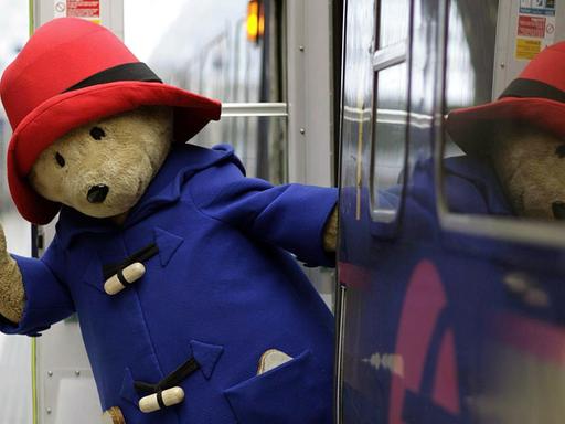 Ankunft von Bär Paddington in der Londoner Paddington Station. Der Bär lehnt aus dem Zug und winkt.