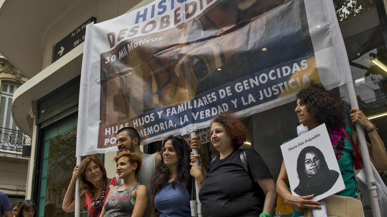 Demonstrant*innen mit Banner. Eine Frau hält das Portrait eines Opfers der Militärdiktatur in Argentinien in ihren Händen. Demonstrant*innen mit Banner. Eine Frau hält das Portrait eines Opfers der Militärdiktatur in Argentinien in ihren Händen.