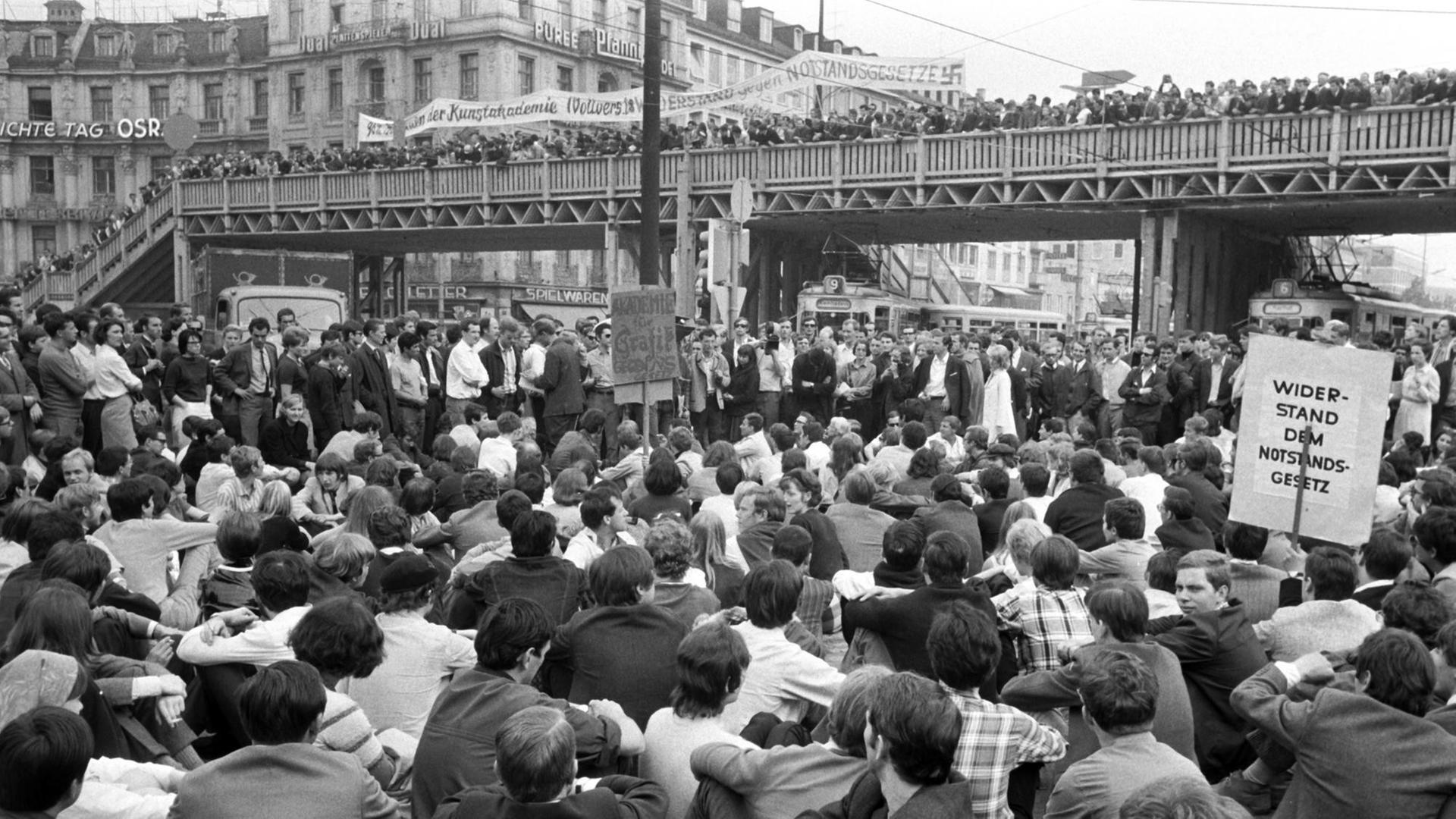 Dichtgedrängt stehen Demonstranten auf der Fußgänger-Notbrücke über dem Münchner Stachus; die Straßenbahnen wurden von den sitzenden Demonstranten blockiert. Am 29.05.1968, dem Vortag der dritten Lesung der Notstandsgesetze im Bonner Bundestag, demonstrierten in München tausende Studenten, Schüler, Arbeiter und Angestellte. Dichtgedrängt stehen Demonstranten auf der Fußgänger-Notbrücke über dem Münchner Stachus; die Straßenbahnen wurden von den sitzenden Demonstranten blockiert. Am 29.05.1968, dem Vortag der dritten Lesung der Notstandsgesetze im Bonner Bundestag, demonstrierten in München tausende Studenten, Schüler, Arbeiter und Angestellte.
