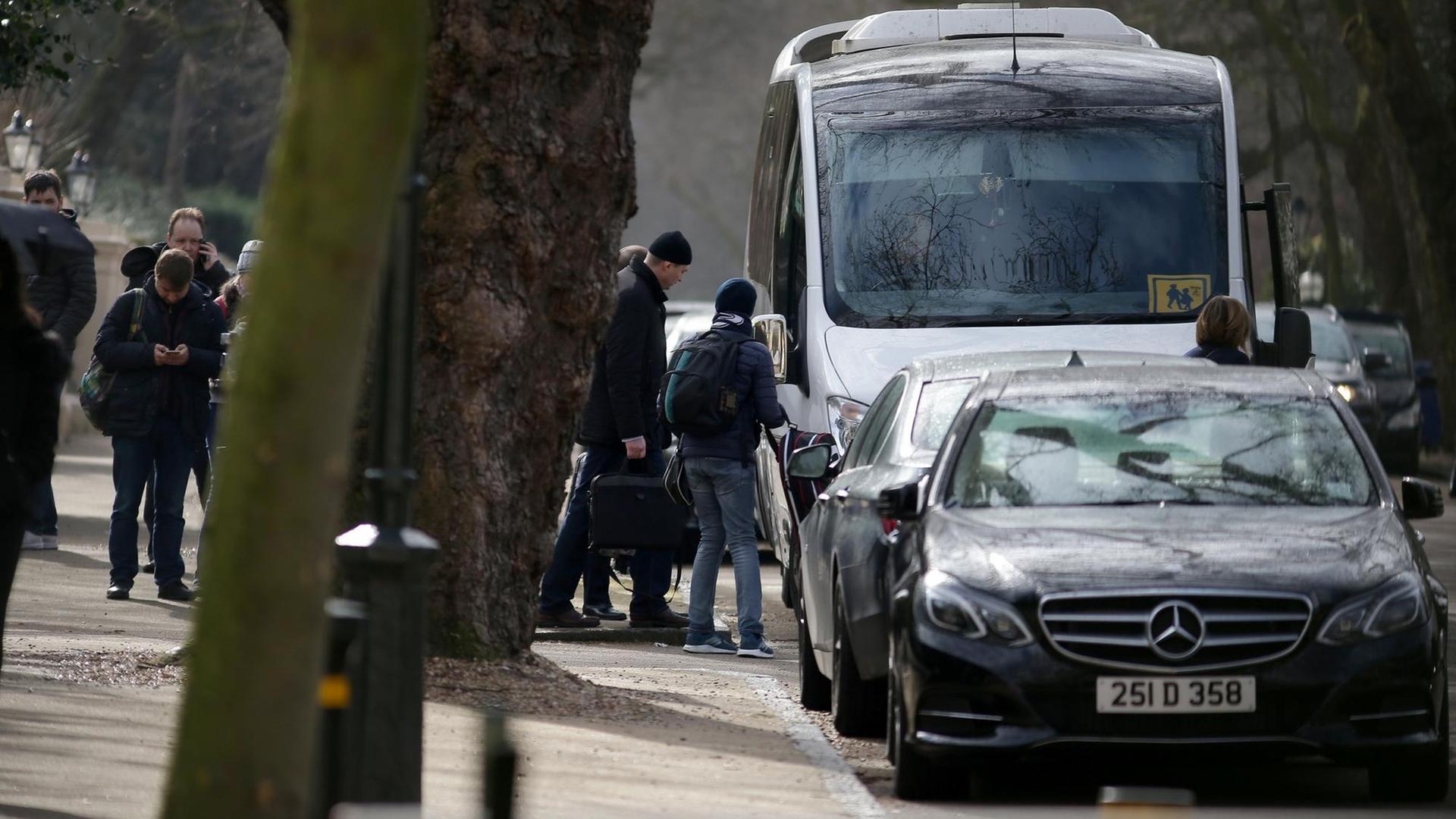 Das Bild zeigt Menschen, die die russische Botschaft in London mit Gepäck verlasssen und einen Bus besteigen.