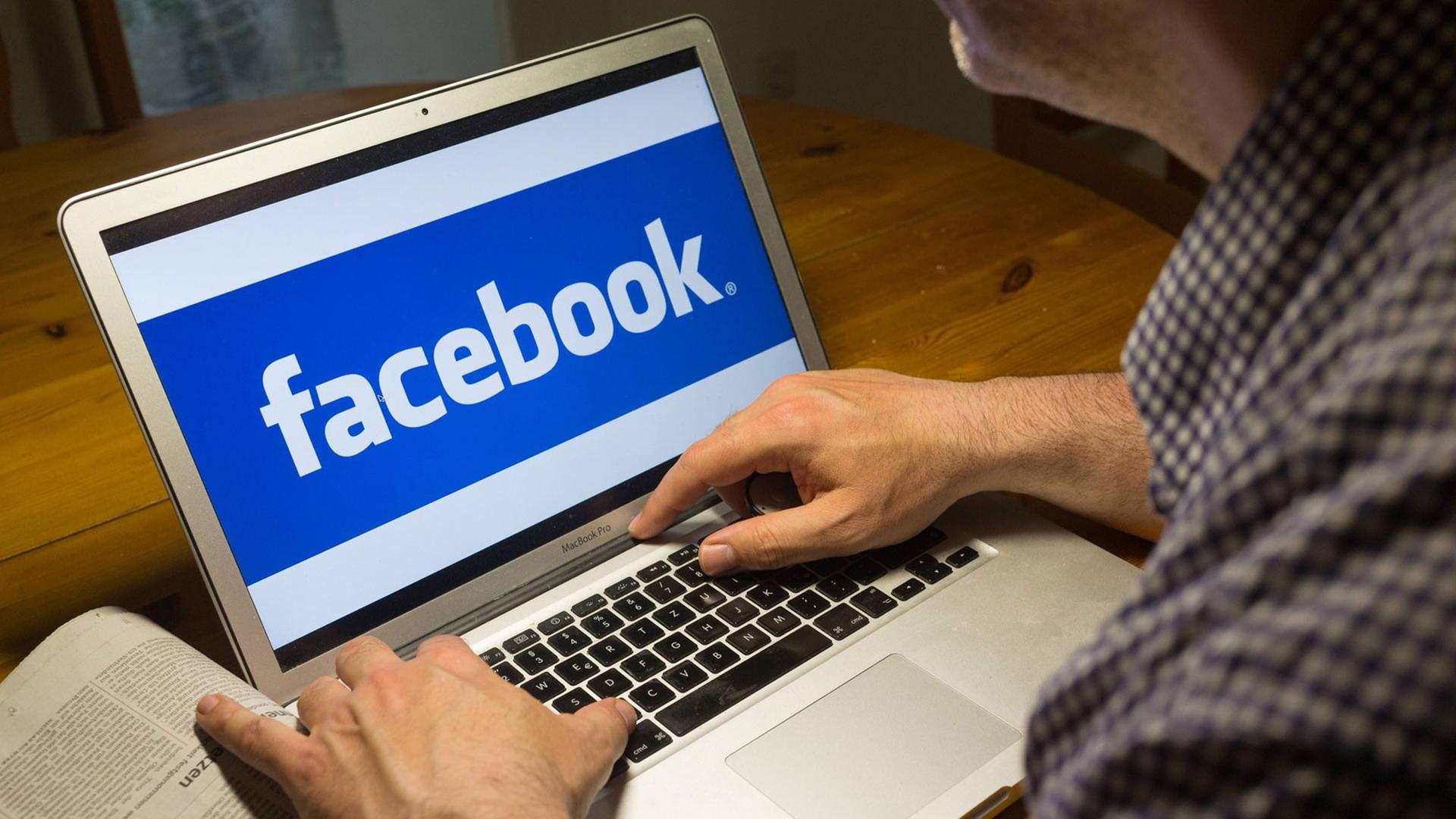 Computernutzer sitzt am Laptop mit dem Logo des sozialen Netzwerks Facebook Computernutzer sitzt am Laptop mit dem Logo des sozialen Netzwerks Facebook