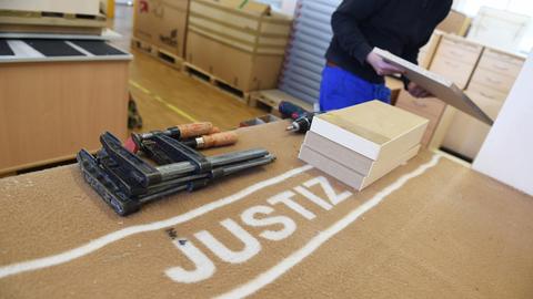 Ein Häftling baut in der Schreinerei der Justizvollzugsanstalt in Ulm (Baden-Württemberg) einen Schrank zusammen, während im Vordergrund mehrere Werkzeuge auf einer Decke liegen, auf der "Justiz" steht.