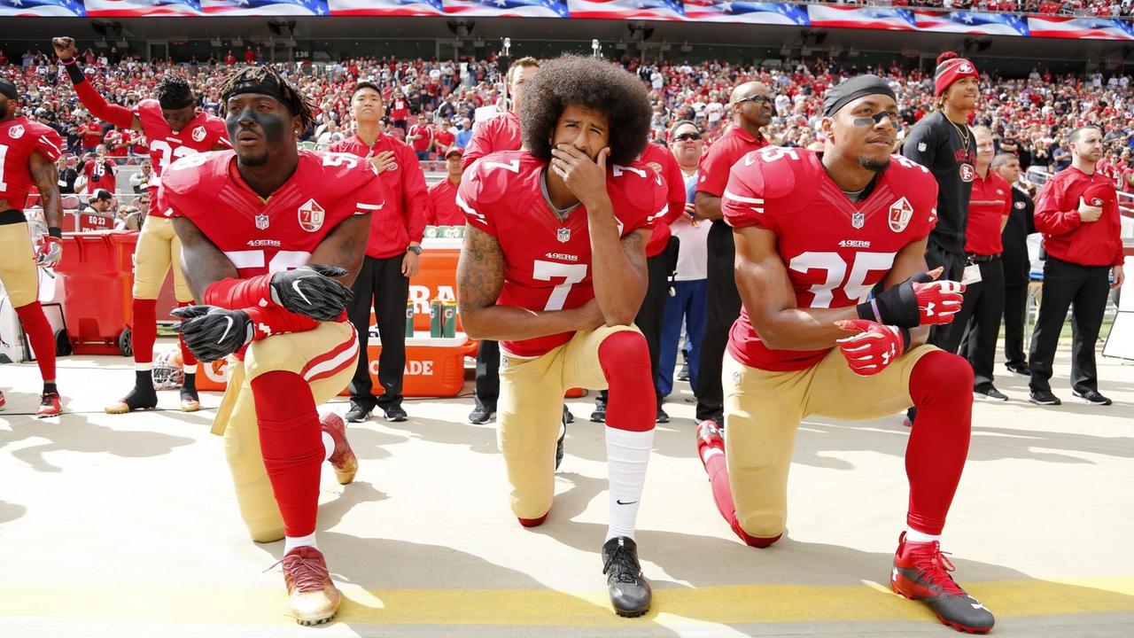Der Quaterback Colin Kaepernick (Mitte) von den San Francisco 49ers und zwei Mitspieler knien während der Nationalhymne bei einem Match der National Football League. Der Quaterback Colin Kaepernick (Mitte) von den San Francisco 49ers und zwei Mitspieler knien während der Nationalhymne bei einem Match der National Football League.