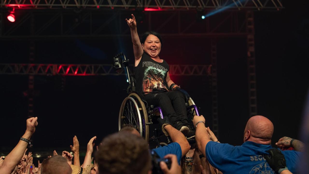 Wacken Open Air 2018, Frau im Rollstuhl steht am Bühnenrand vor begeistertem Publikum, im Hintergrund eine dunkle Bühne Wacken Open Air 2018, Frau im Rollstuhl steht am Bühnenrand vor begeistertem Publikum, im Hintergrund eine dunkle Bühne