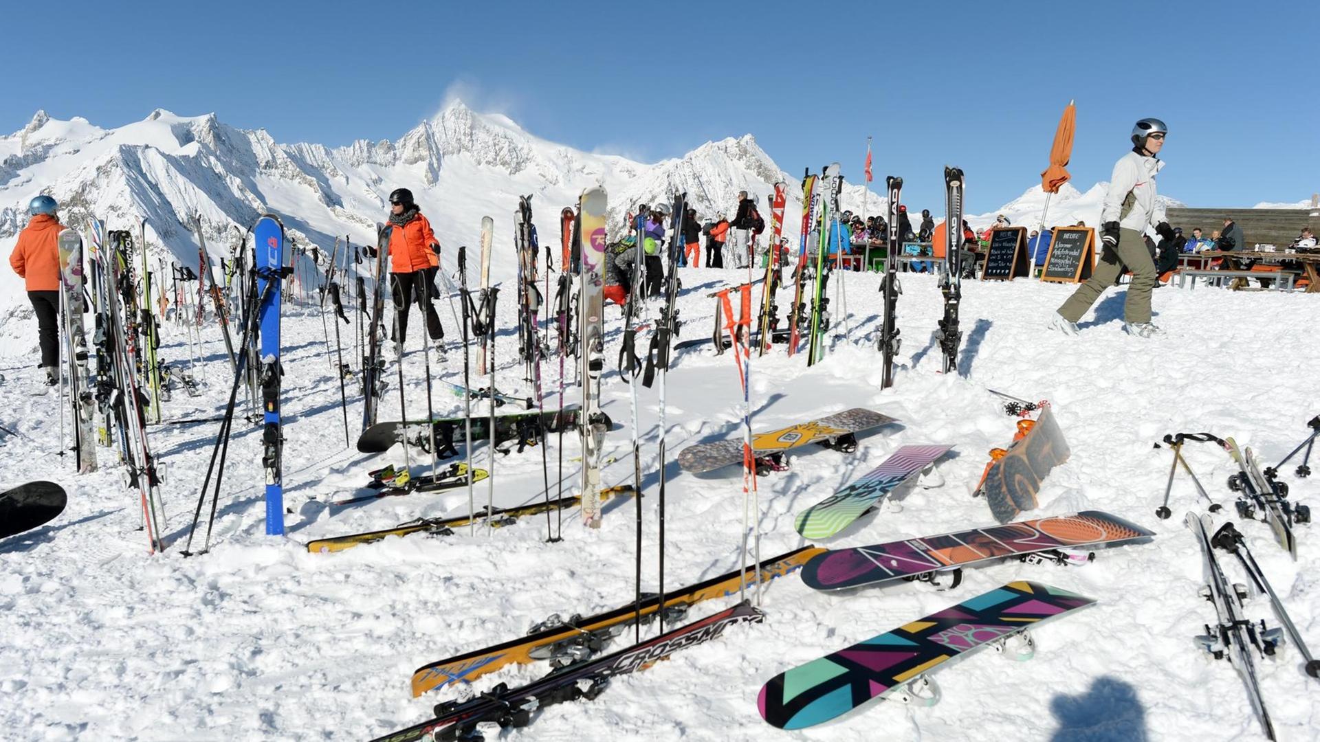Auf einer schneebedeckten Landschaft stehen mehrere Skifahrer, im Vordergrund liegen Skier und Snowboards. Auf einer schneebedeckten Landschaft stehen mehrere Skifahrer, im Vordergrund liegen Skier und Snowboards.