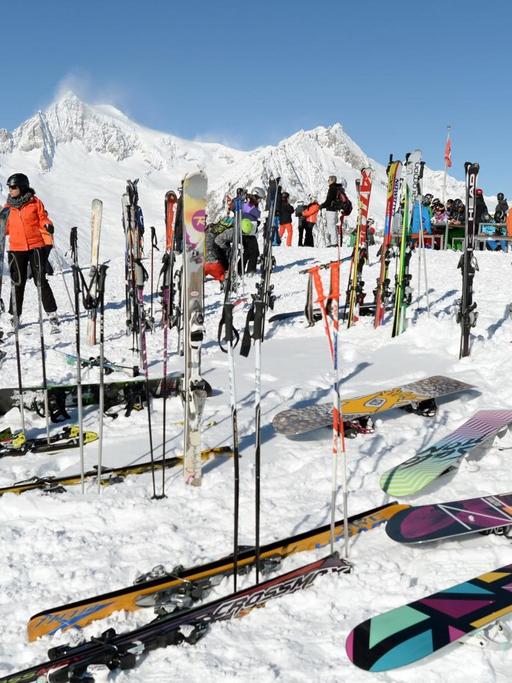 Auf einer schneebedeckten Landschaft stehen mehrere Skifahrer, im Vordergrund liegen Skier und Snowboards.