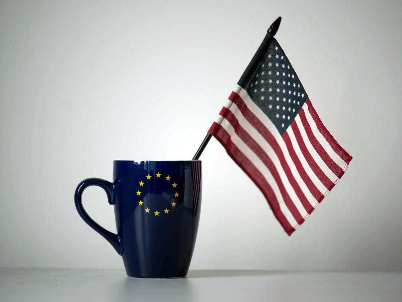 In einer Tasse mit einem EU-Symbol steckt eine US-Fahne, aufgenommen  in einem Büro in Dresden.
